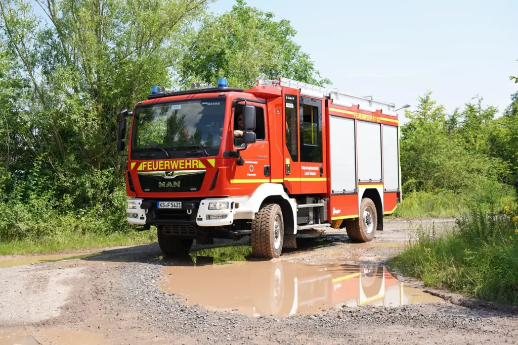 Löschfahrzeug der Freiwilligen Feuerwehr Hertingshausen fährt auf einem Feldweg an einem tiefen Wasserloch vorbei.