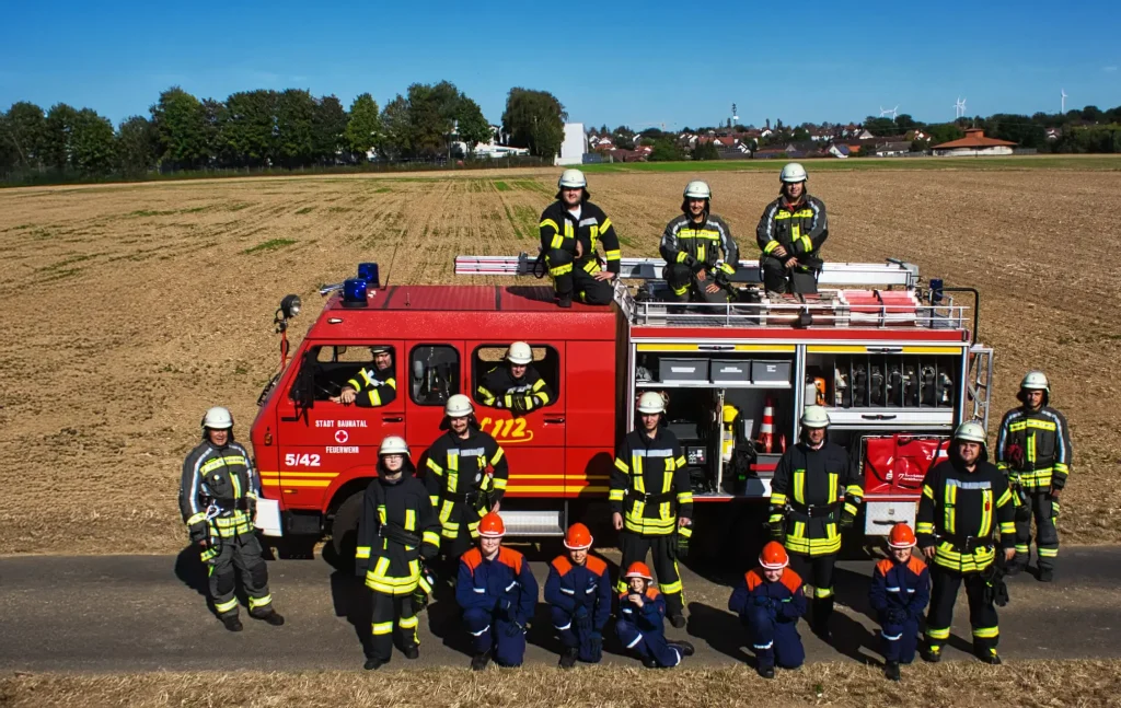 Feuerwehrfahrzeug der Freiwilligen Feuerwehr Baunatal-Hertingshausen mit Einsatzabteilung und Jugendfeuerwehr davor.