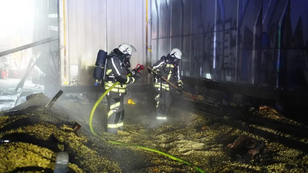 Zwei Feuerwehrmänner räumen eine ausgebrannte Lagerhalle auf.