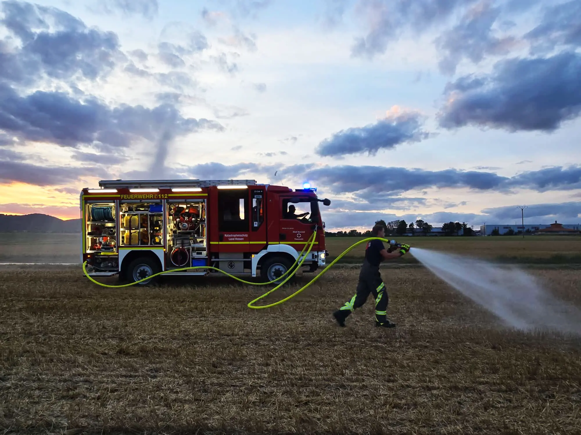 Feuerwehrfrau der Freiwilligen Feuerwehr Hertingshausen befeuchtet ein trockenes Feld mit einem Strahlrohr.