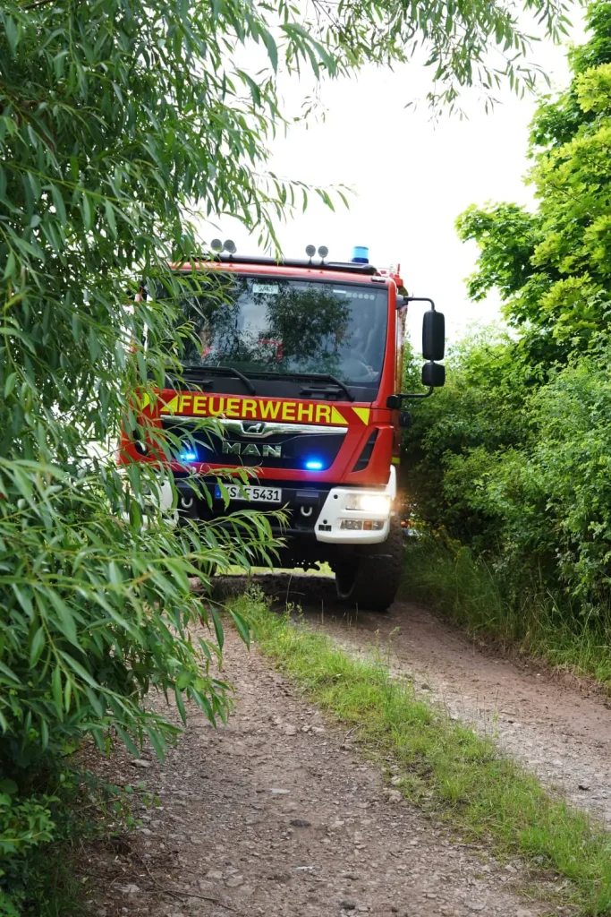 Löschfahrzeug der Freiwilligen Feuerwehr Hertingshausen auf einem Feldweg, teilweise von Büschen verdeckt.