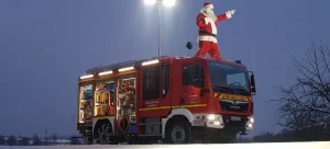 Ein Nikolaus steht auf dem Löschfahrzeug der Freiwilligen Feuerwehr Hertingshausen und zeigt nach vorne.