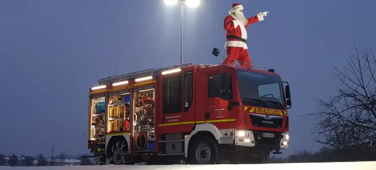 Ein Nikolaus steht auf dem Löschfahrzeug der Freiwilligen Feuerwehr Hertingshausen und zeigt nach vorne.